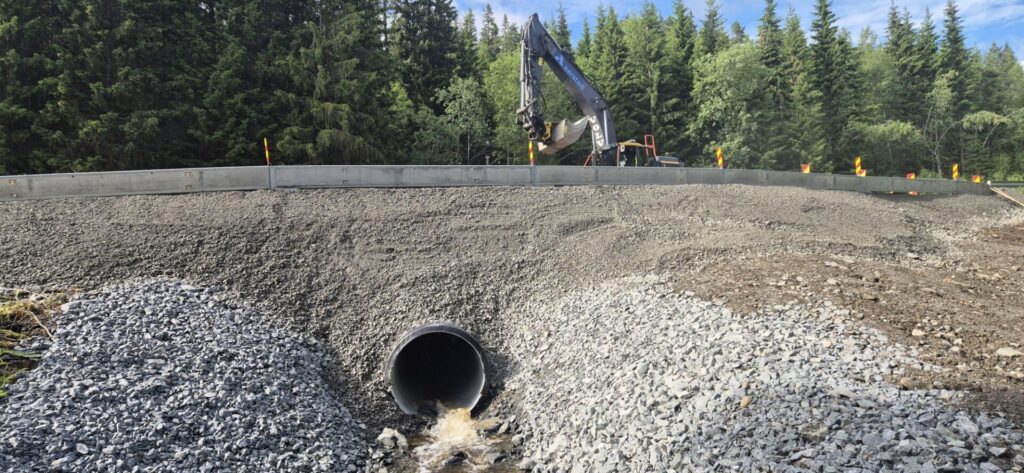 Foto av gravemaskin som arbeider på vei med skråning i forgrunnen og skog i bakgrunnen